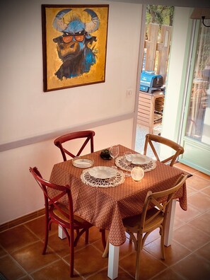 Une table à manger recouverte d’une nappe à motifs, quatre chaises en bois et une œuvre d’art encadrée accrochée au mur.