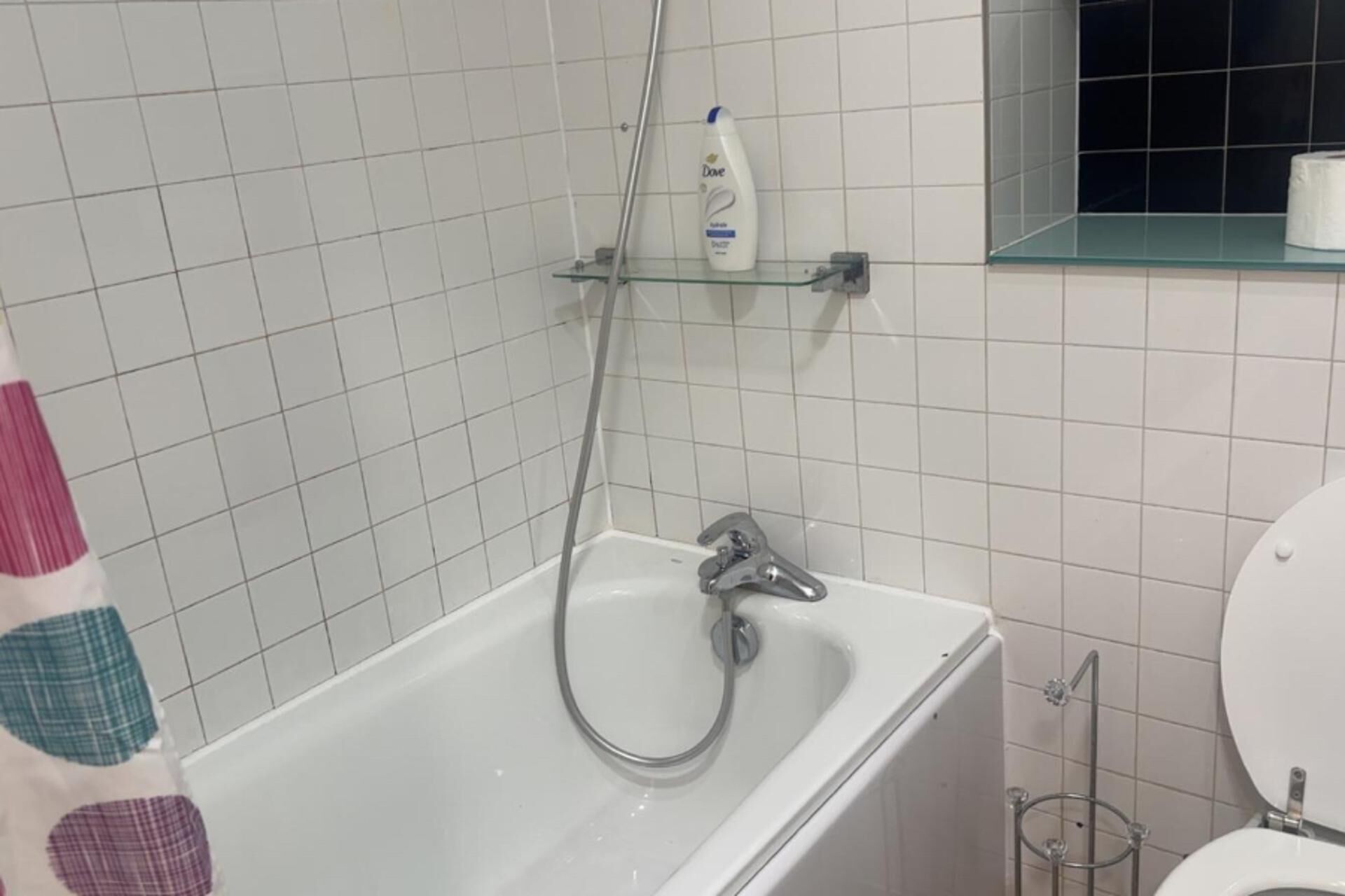 Ein Badezimmer mit Badewanne, Dusche und Toilette. Auf einem Regal über der Wanne steht eine Flasche Dove Seife.
