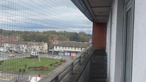 A balcony with a view of a town, a grassy area, and a road. - London 1 Bed Apartment Close to Barking Station (Barking)