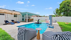 Un jardin avec une piscine, des chaises longues, un patio couvert et un bar de style polynésien.