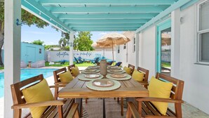 Un espace extérieur abrité où l’on peut prendre ses repas, avec une piscine en arrière-plan.