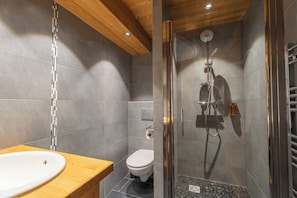 A modern bathroom with a wooden vanity, a toilet, and a glass-enclosed shower area. - Apartment Le Cosy (Les Gets)