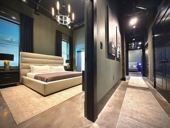 A modern bedroom with a large bed, a chandelier, and a hallway leading to another room.