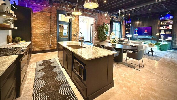 Una cocina moderna con una isla central, una zona de comedor con sillas y un televisor al fondo.