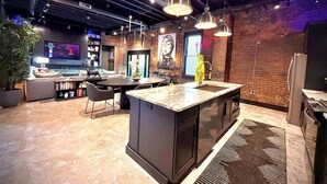 Una cocina moderna con una isla central, iluminación colgante y pared de ladrillo.