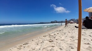 Una playa con gente caminando y sentada, cielo despejado y orilla arenosa.