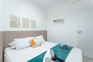 A hotel room with a bed, pillows, a towel, a hairdryer, and wall art. - Temporada Prime - Praia (Rio de Janeiro)