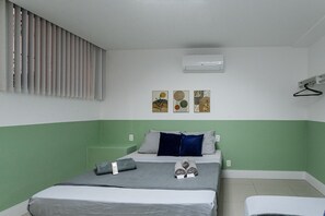 Ett hotellrum med en säng, en väggmonterad luftkonditioneringsanläggning och tre inramade konstverk.