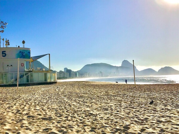A beach with a lifeguard tower, clear skies, and distant mountains.