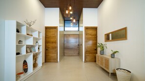 Un couloir avec une porte en bois, des étagÚres blanches, une console ornée de plantes et des luminaires suspendus.