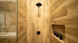 Une douche avec un mur recouvert de panneaux en bois, une pomme de douche circulaire et une étagÚre avec des bouteilles.