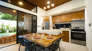 A modern kitchen with a dining area, wooden cabinets, stainless steel appliances, and a view of a swimming pool.