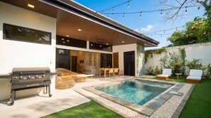 A modern outdoor pool area with a barbecue grill, seating, and a covered patio.
