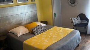 A bedroom with a bed, a chair, a wall-mounted mirror, and a hanging light fixture. - Hôtel Restaurant Le Pont de l'Aube (Arcis-sur-Aube)