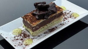 A slice of layered dessert on a white plate on a glass table. - Hôtel Restaurant Le Pont de l'Aube (Arcis-sur-Aube)