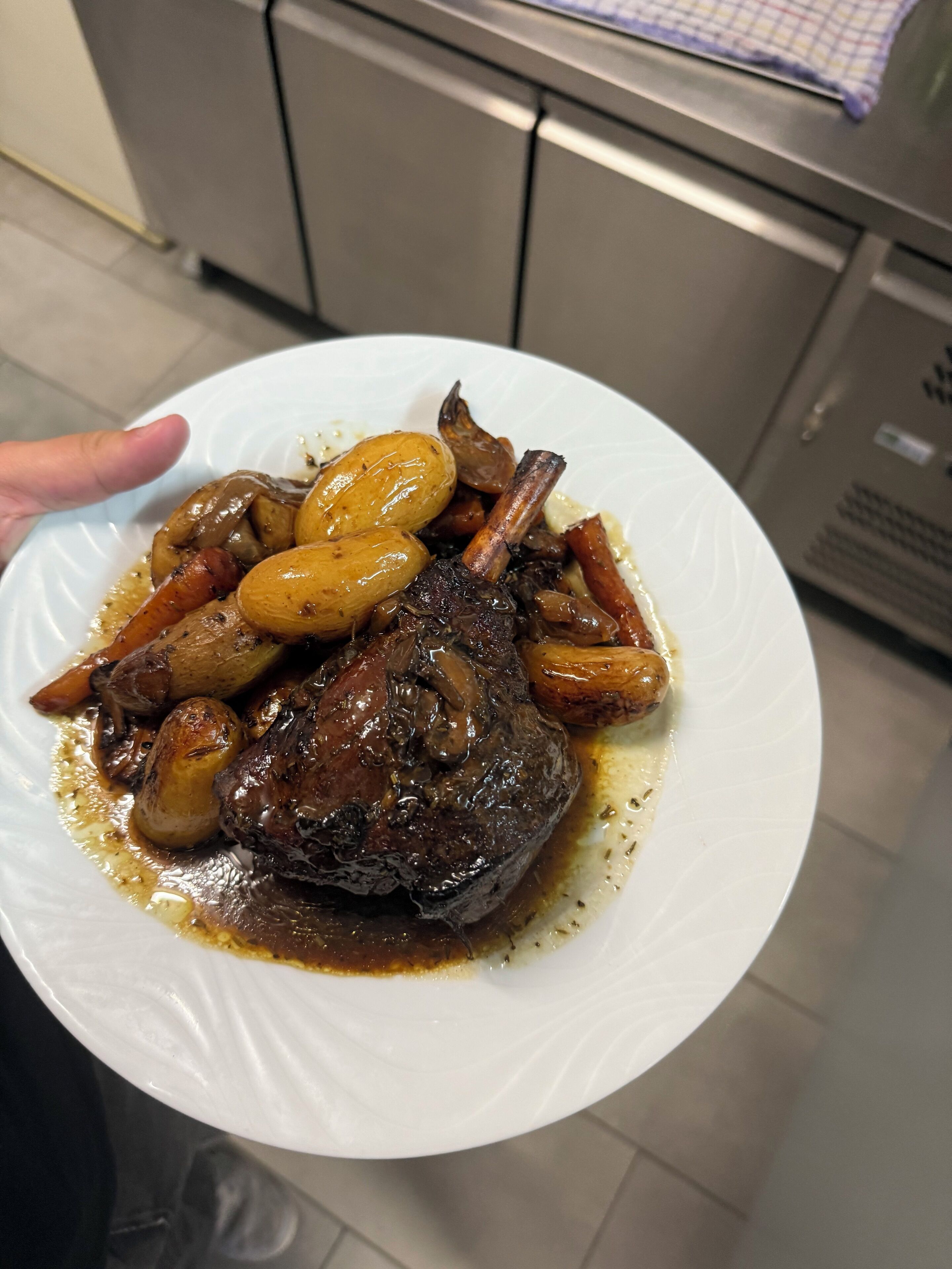 A plate of food with a lamb shank, mushrooms, and carrots.