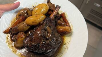 A plate of food with a lamb shank, mushrooms, and carrots.