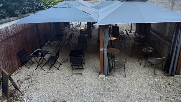 An outdoor seating area with tables and chairs under large umbrellas, surrounded by a gravel ground and a brick wall. - Hôtel Restaurant Le Pont de l'Aube (Arcis-sur-Aube)