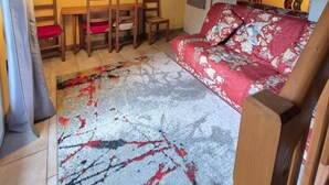 Una stanza accogliente con soffitto in legno, un divano rivestito di fiori, un'area pranzo con sedie e un televisore fissato alla parete.