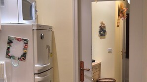 Una cucina con frigorifero, microonde e lavandino. Si apre una porta su un corridoio con un cestino e un piccolo tappeto.