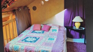 Una camera da letto con soffitto spiovente, un letto con copriletto decorato, un comodino con lampada e un tappeto viola.