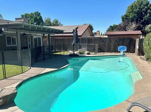 Ein Garten mit Swimmingpool, überdachter Terrasse und Holzzaun.