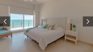 A bedroom with a large bed, a nightstand, a ceiling fan, and a view of the ocean.