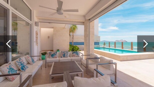 A modern outdoor living area with a pool, white furniture, and a view of the ocean.