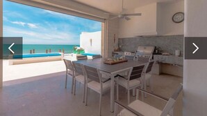 A modern kitchen with a view of the sea, a dining area with a table and chairs, and a ceiling fan.