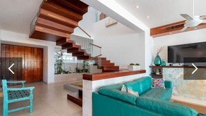 A spacious living area with a teal sofa, wooden staircase, and a flat-screen TV.