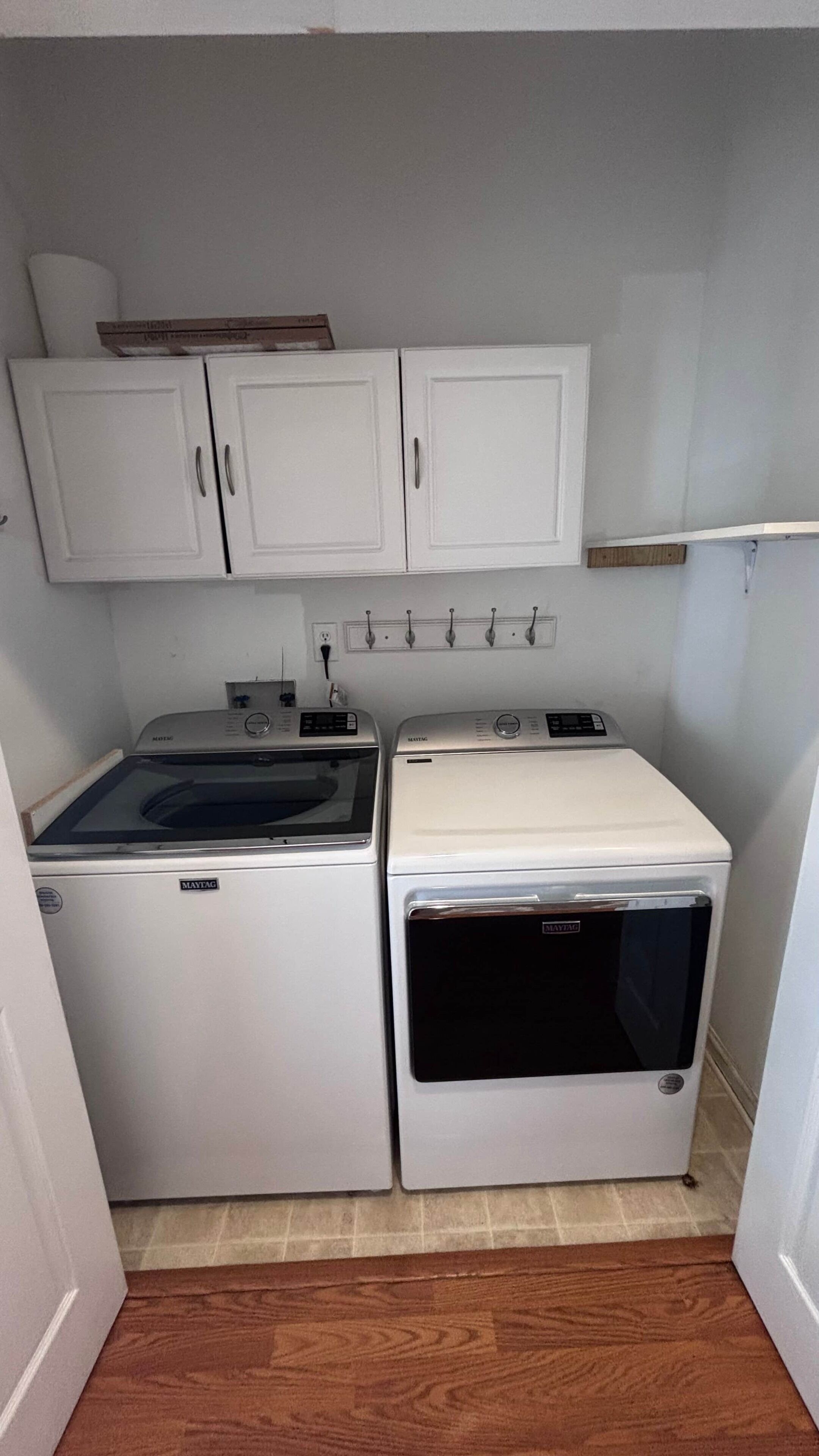 Een kleine wasruimte met twee witte wasmachines, een klein kastje en een wandradiator.