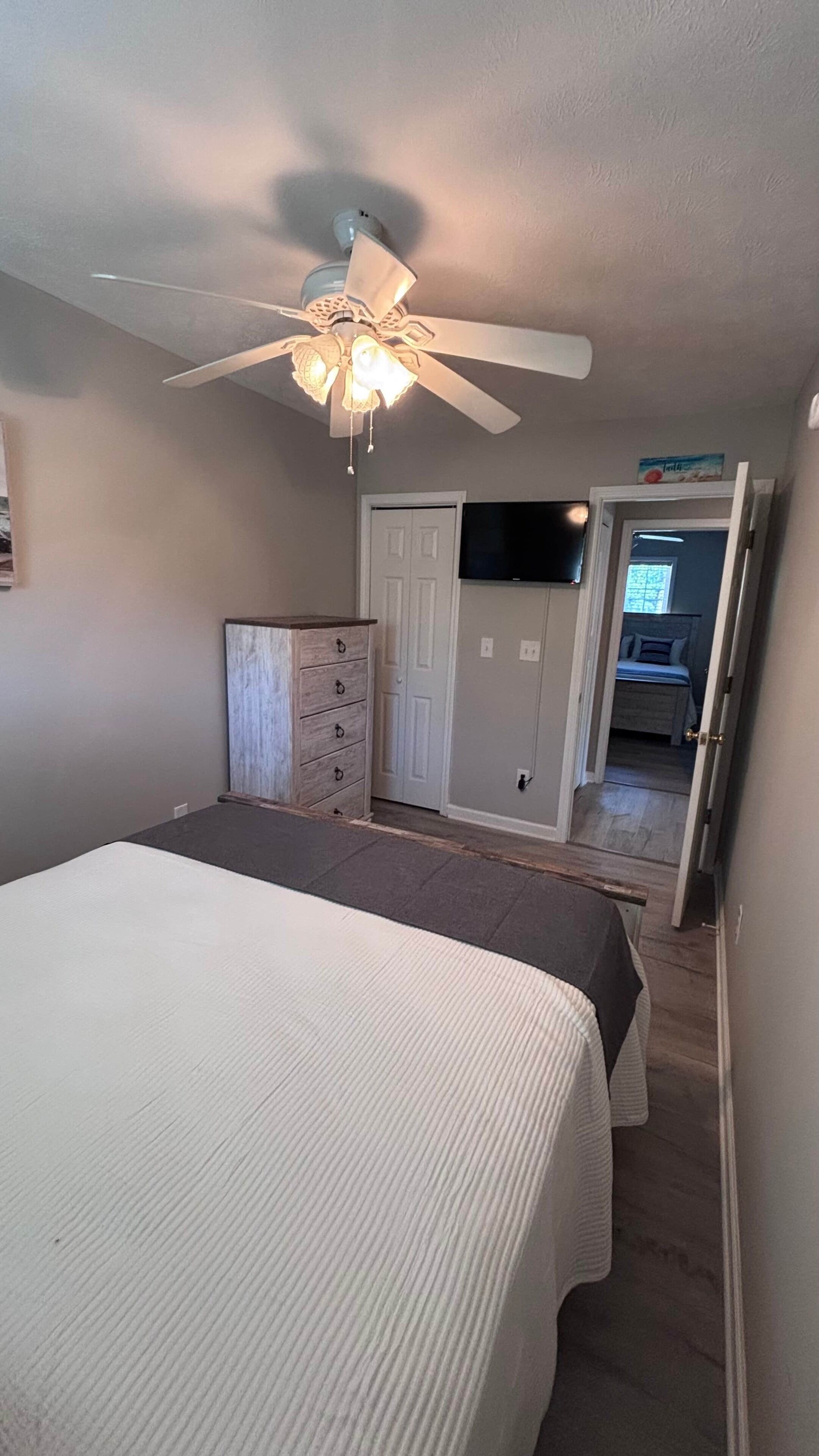 Un dormitorio con cama, cómoda, ventilador de techo y una puerta que da a otra habitación.