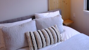 A neatly made bed with white bedding and striped pillows, a wooden slat wall, and a hanging light fixture. - Luxury condo w/ mountain view, close to downtown! (Salida)