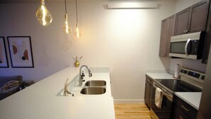 A modern kitchen with a white countertop, stainless steel sink, and dark wooden cabinets. There are pendant lights above the sink and a microwave above the stove. - Luxury condo w/ mountain view, close to downtown! (Salida)