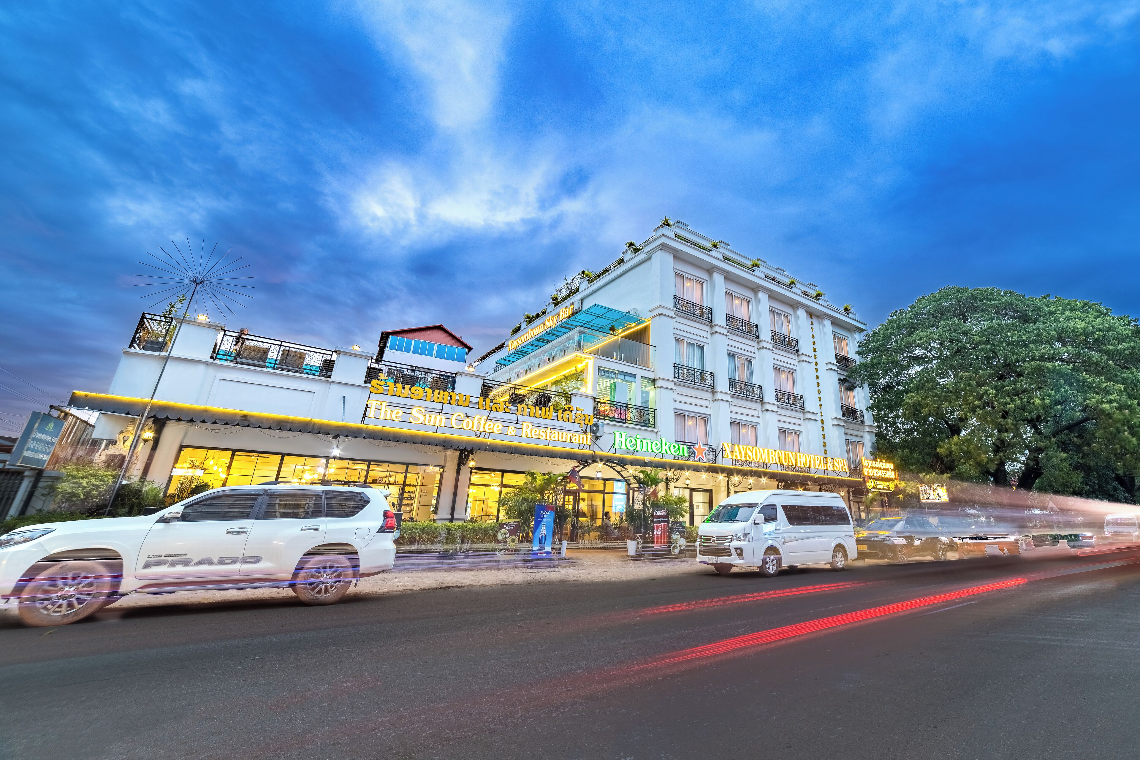 Un hotel de varios pisos con un llamativo letrero de 'Heineken', un 'Sun Coffee & Restaurant' en la planta baja y un letrero de 'Xaysomboun Hotel & Spa'.