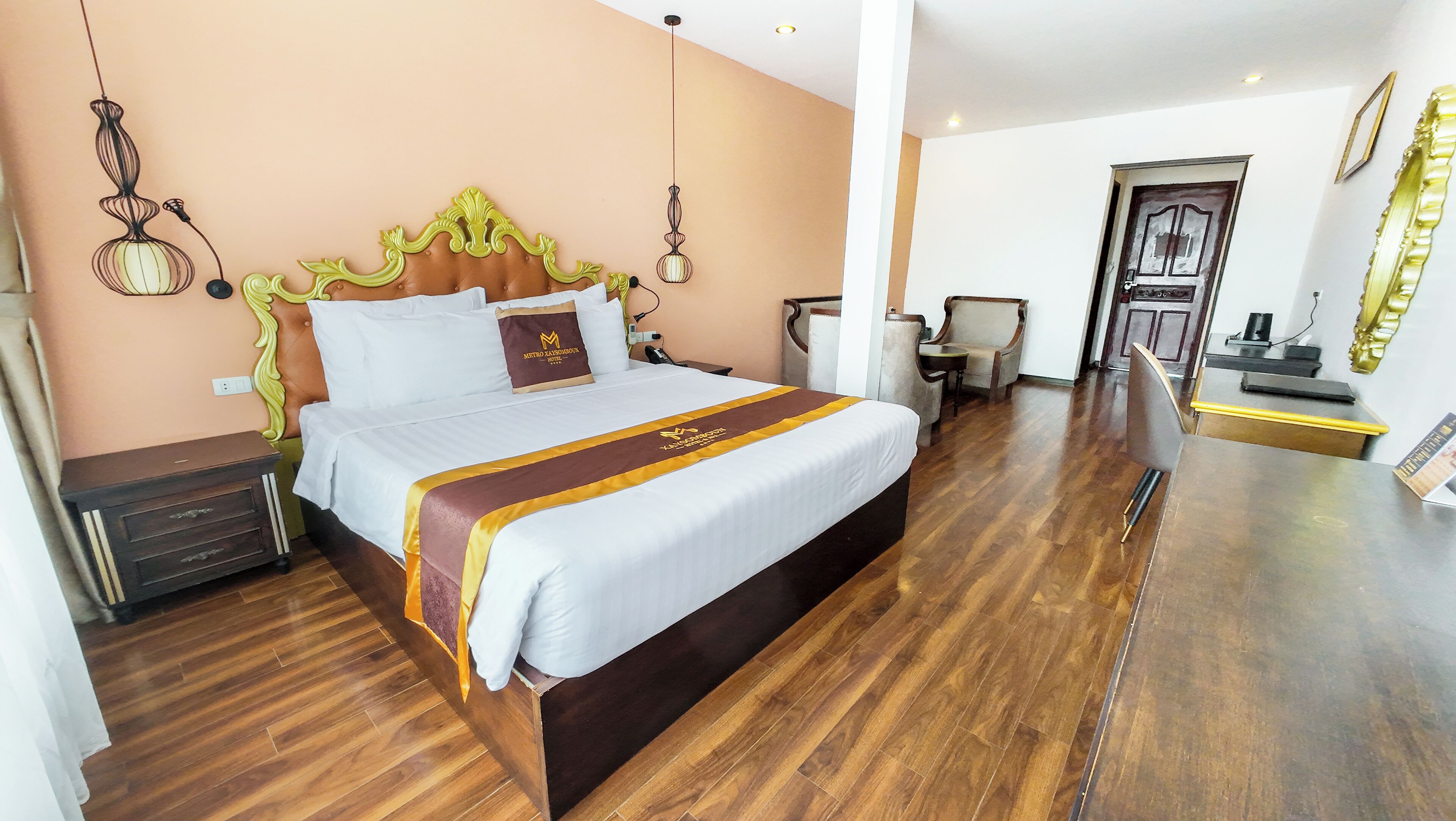 A hotel room with a large bed, wooden flooring, a desk, and a chair.