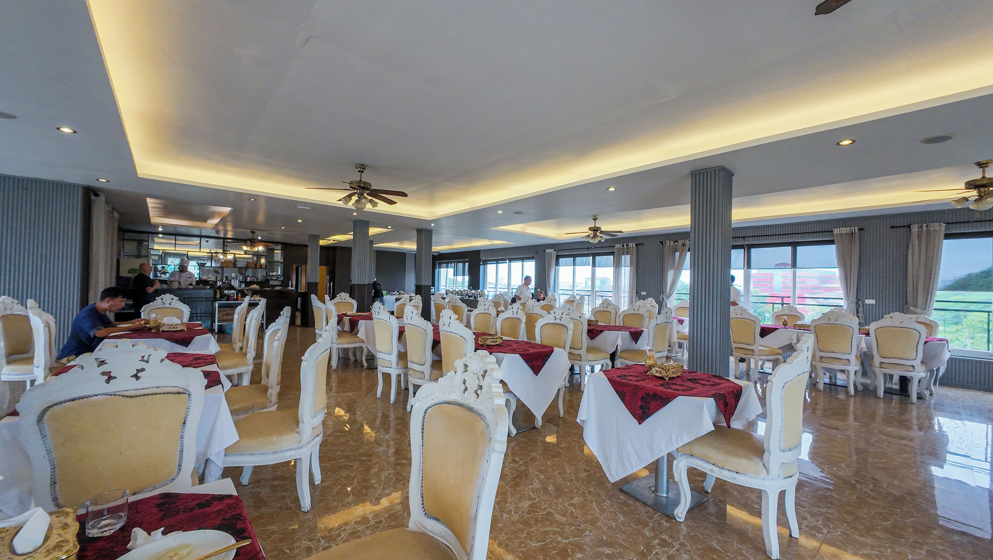 A spacious dining area with rows of white chairs and tables, large windows, and ceiling fans.