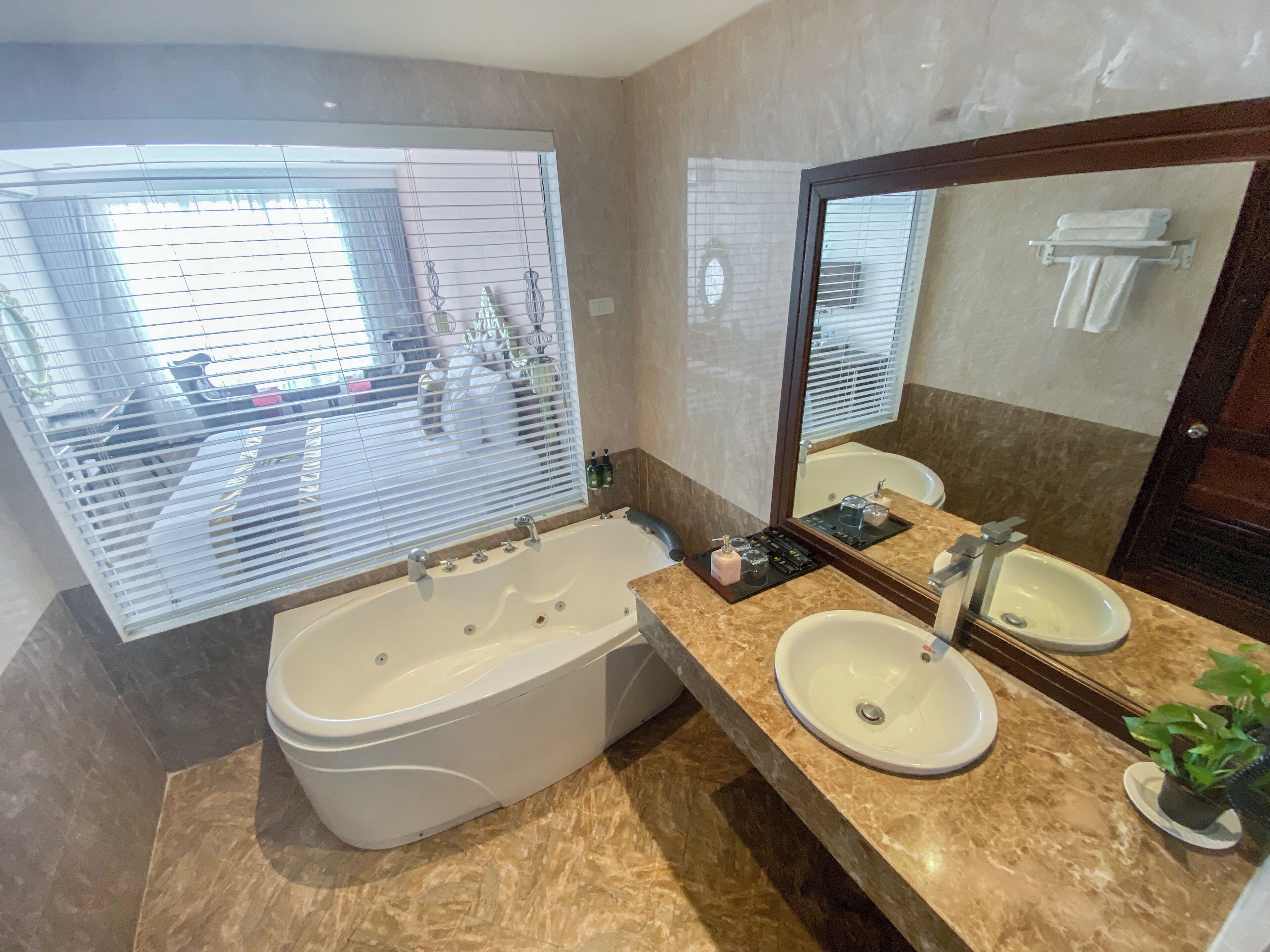 A bathroom with a bathtub, two sinks, a large mirror, and a window with blinds.