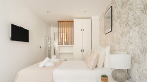 Un dormitorio moderno con una cama, una mesita de noche con lámpara, un televisor montado en la pared y un armario con espejo.