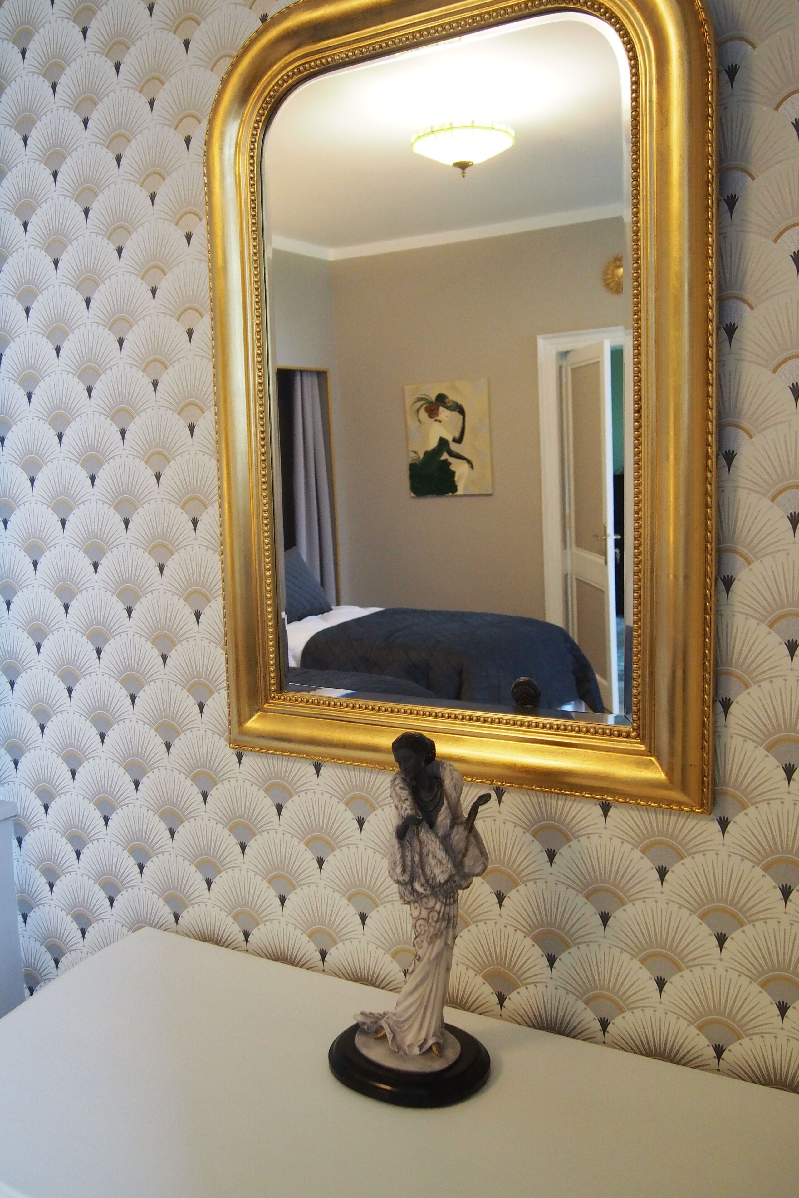 Une pièce avec un grand miroir, un lit et une statue posée sur une table.