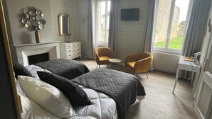 A bedroom with two beds, a desk, a chair, and a window with a view of greenery.