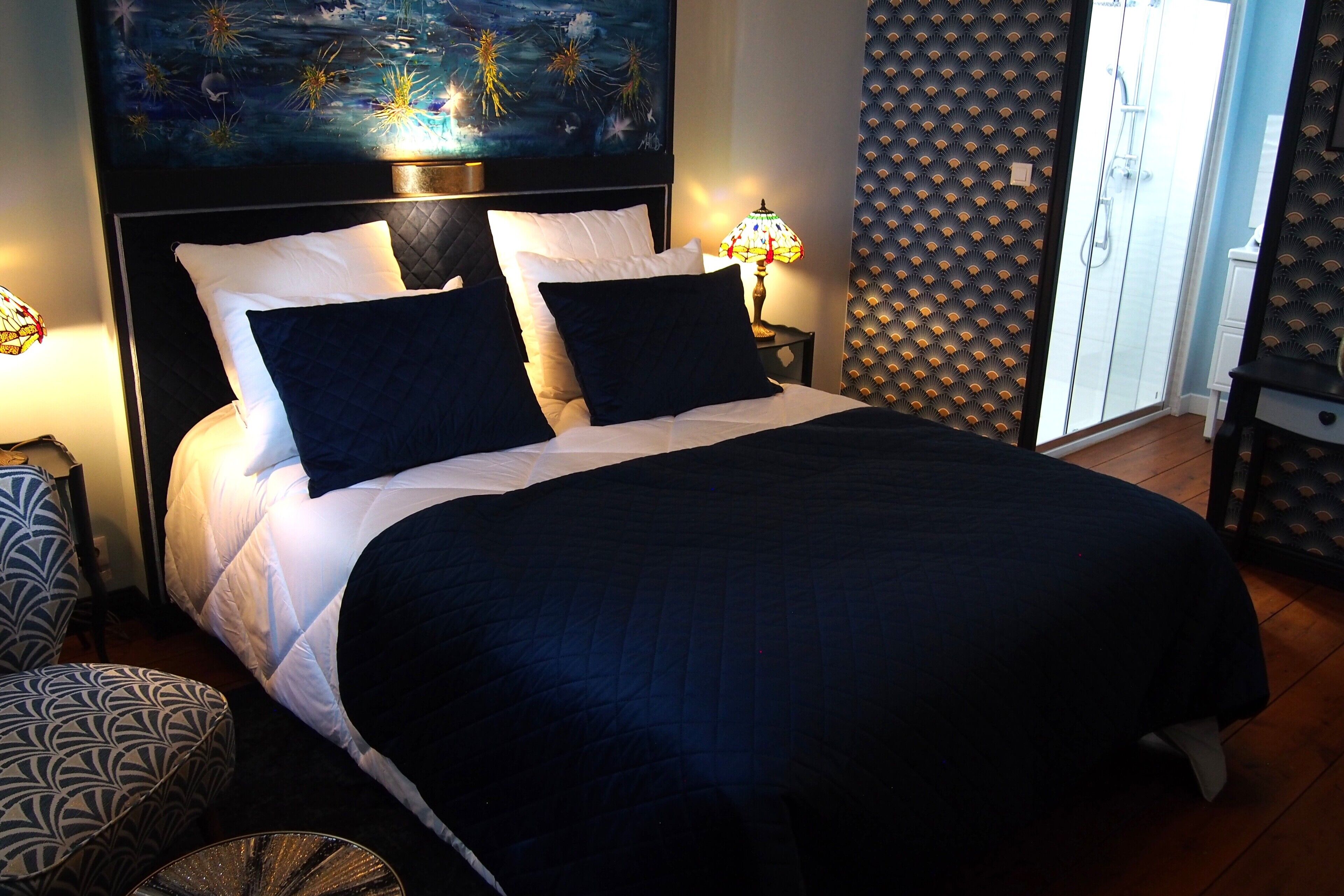 Una cama bien hecha con una colcha azul oscuro y almohadas blancas, con dos lámparas de noche a cada lado.
