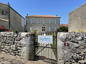 A stone wall with a gate leading to a building with a tiled roof and multiple windows. - Le Rococo (Couquèques)