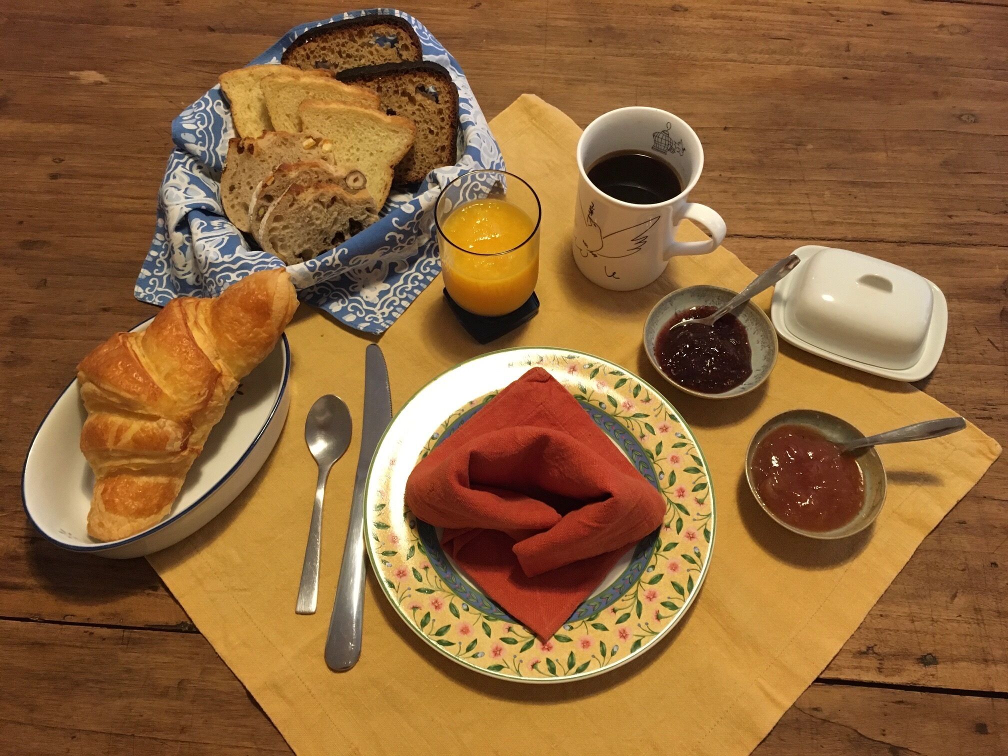 A breakfast table with bread, croissant, juice, coffee, jam, and a napkin.
