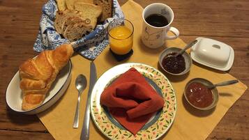A breakfast table with bread, croissant, juice, coffee, jam, and a napkin.