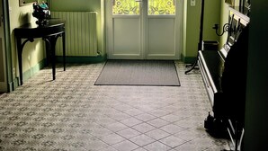 Una habitación con suelo de baldosas, un radiador, un perchero y un piano.
