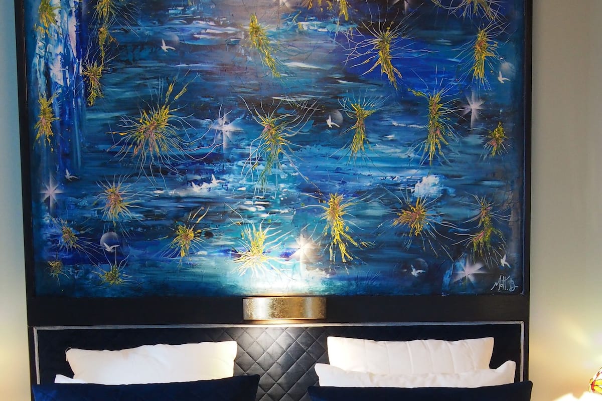 A hotel room with a large bed, two pillows, a headboard, and a wall painting.