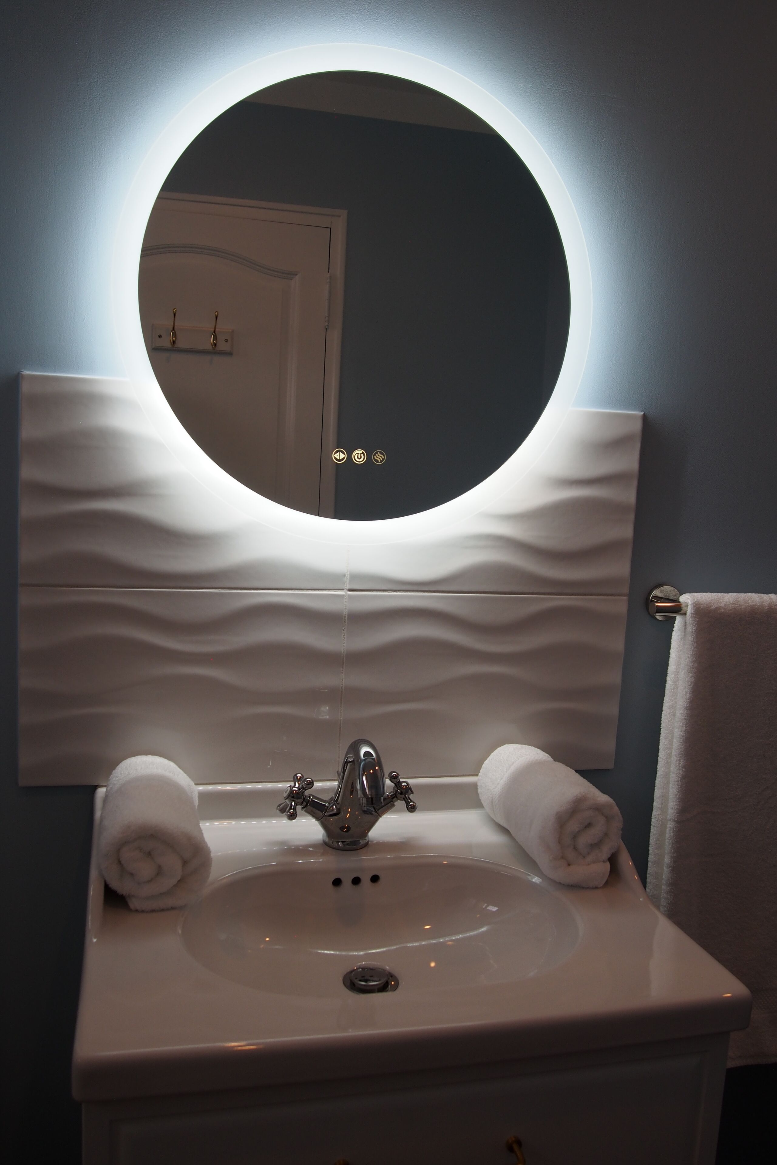 Une salle de bain avec un miroir rond, un lavabo et deux serviettes.