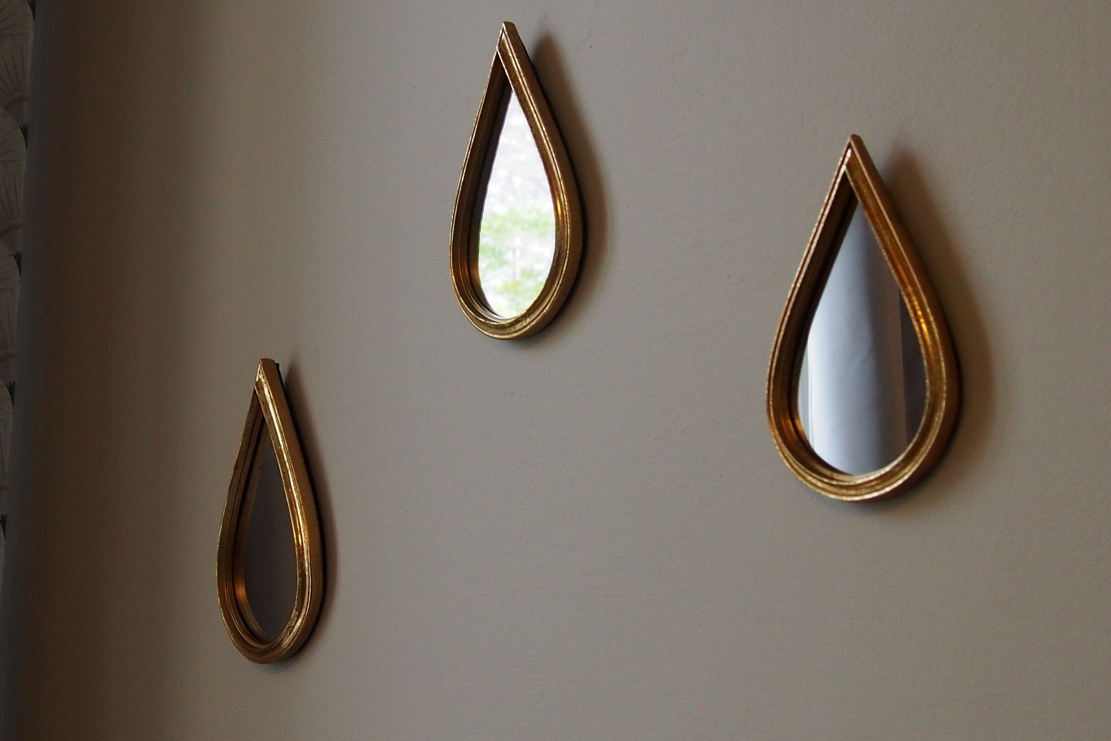 Trois miroirs en forme de goutte d’eau, fixés au mur et dotés de cadres dorés.