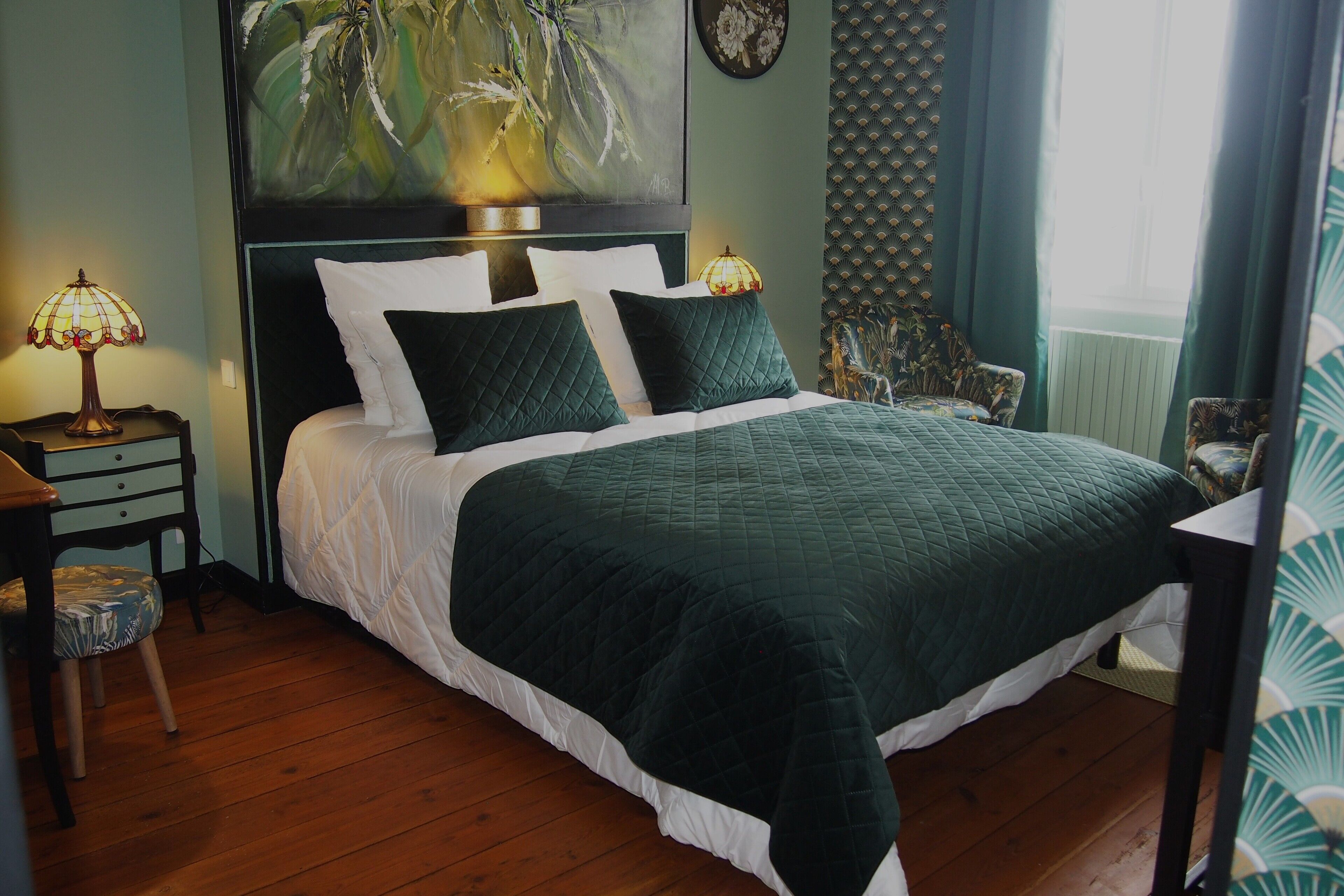 A neatly made bed with a green quilt, a nightstand with a lamp, and a chair with a patterned cushion.